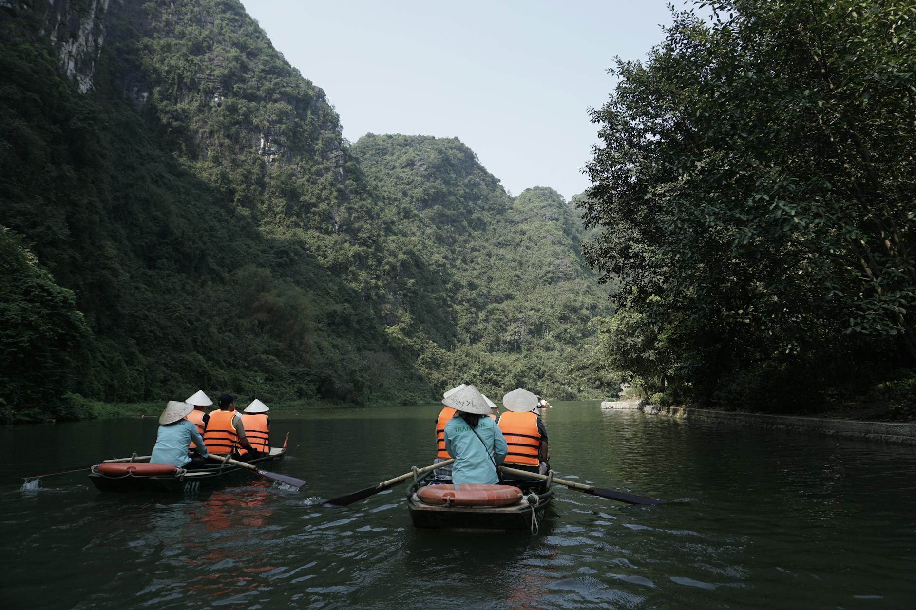 Tourists in rowboats on a serene river in Ninh Bình, Vietnam, surrounded by lush green mountains.