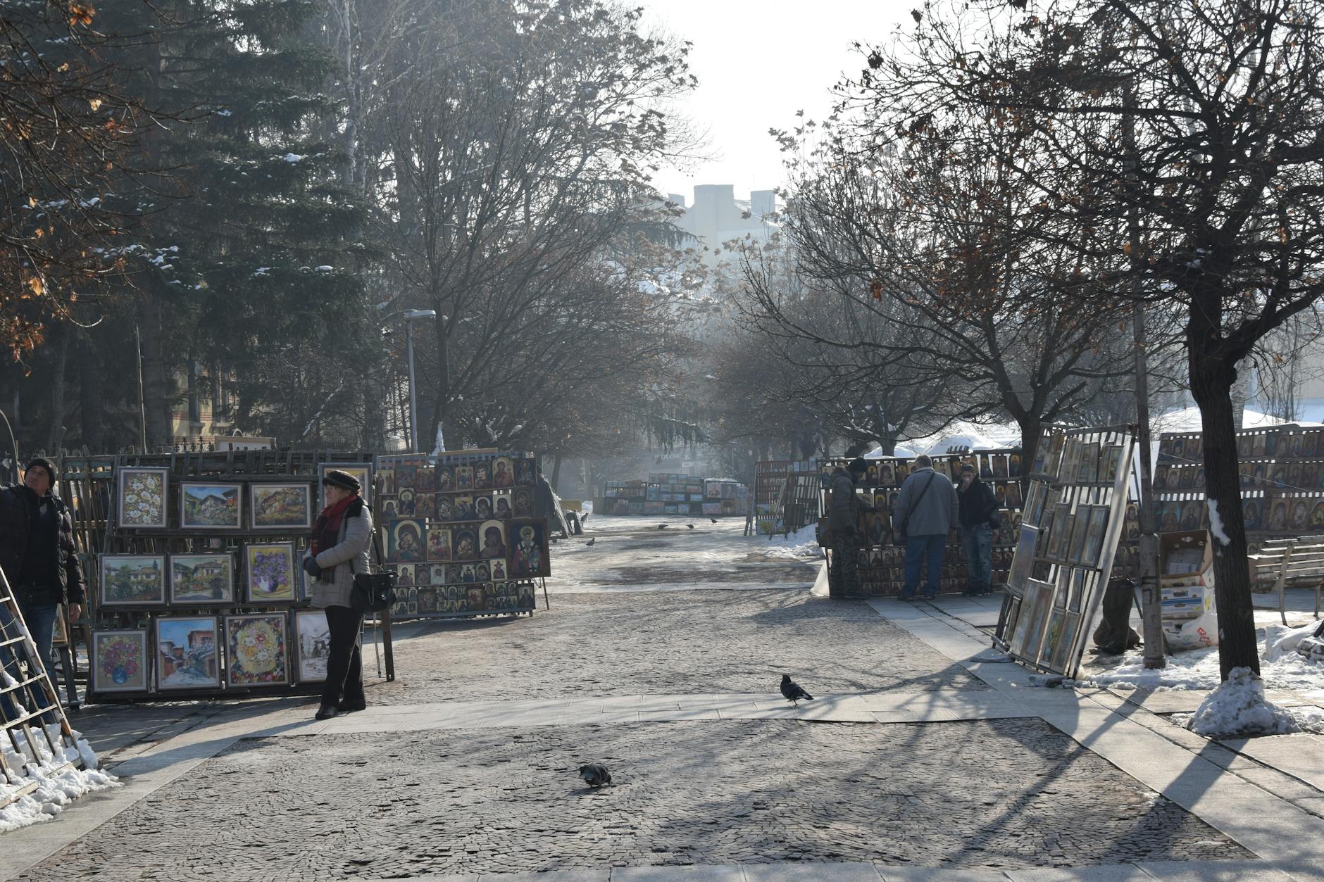 Winter scene of an outdoor art market in Sofia with paintings on display.