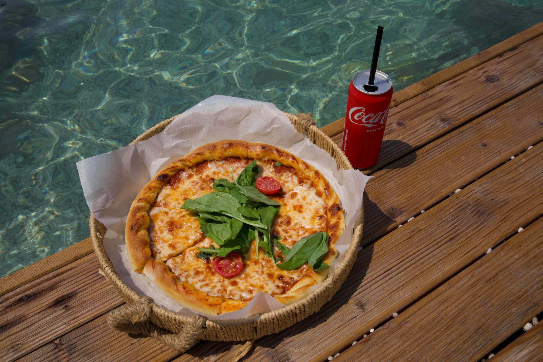 Delicious cheese pizza with arugula and tomato by a serene poolside, perfect for a sunny day.