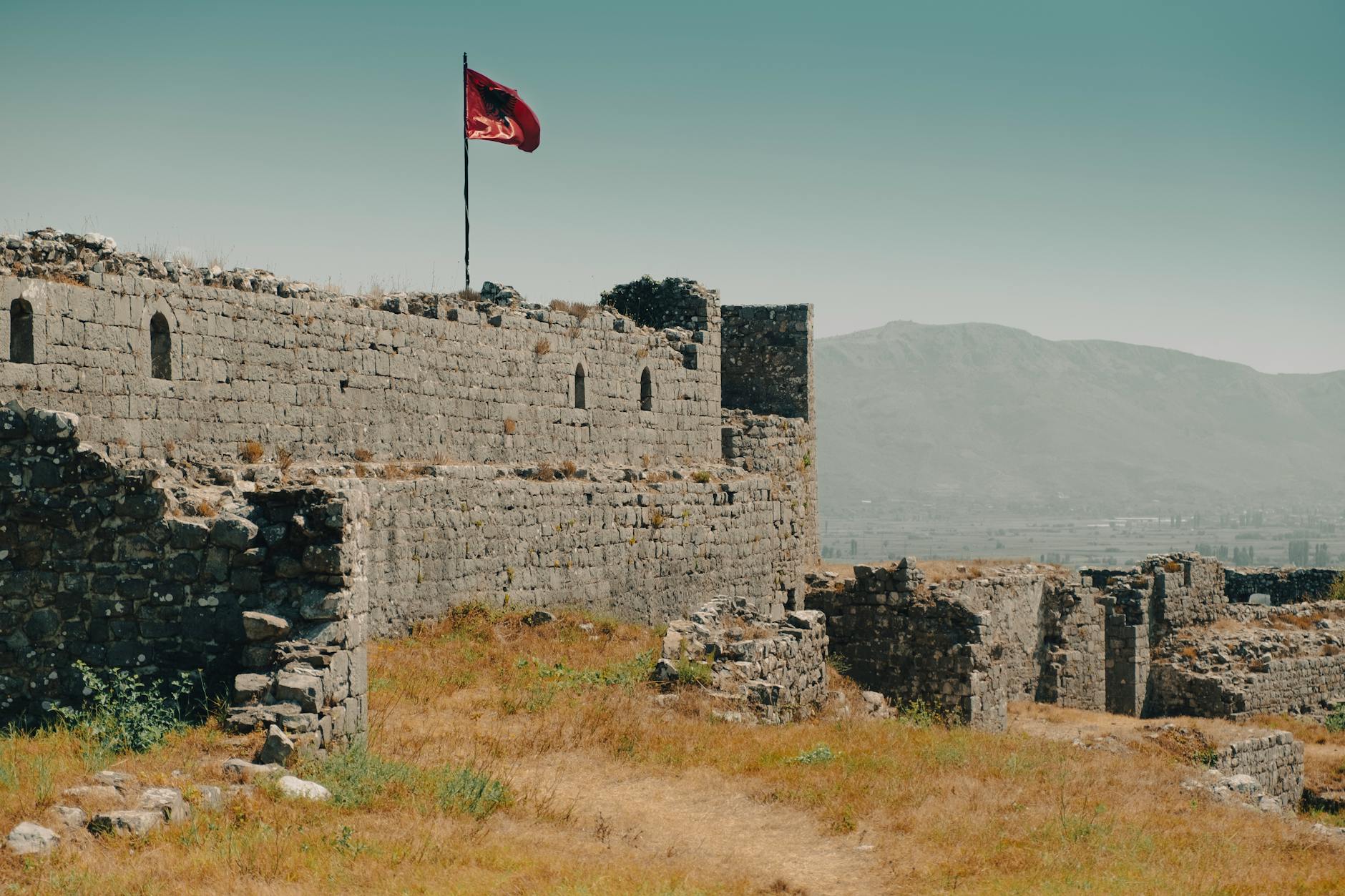 Historic Shkodra Castle ruins with Albanian flag, overlooking mountains.