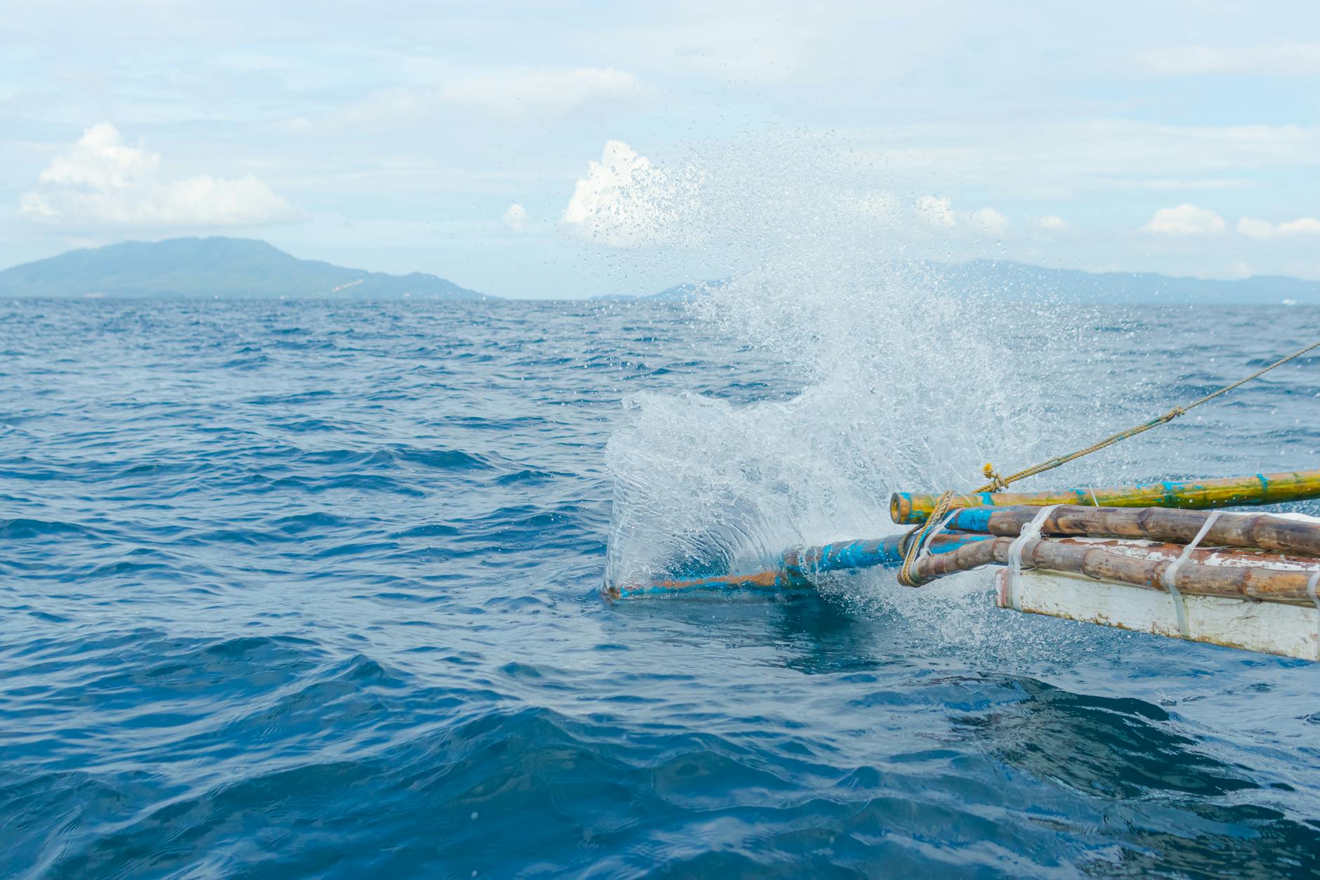A traditional wooden canoe splashes through vibrant ocean waters under a clear sky.