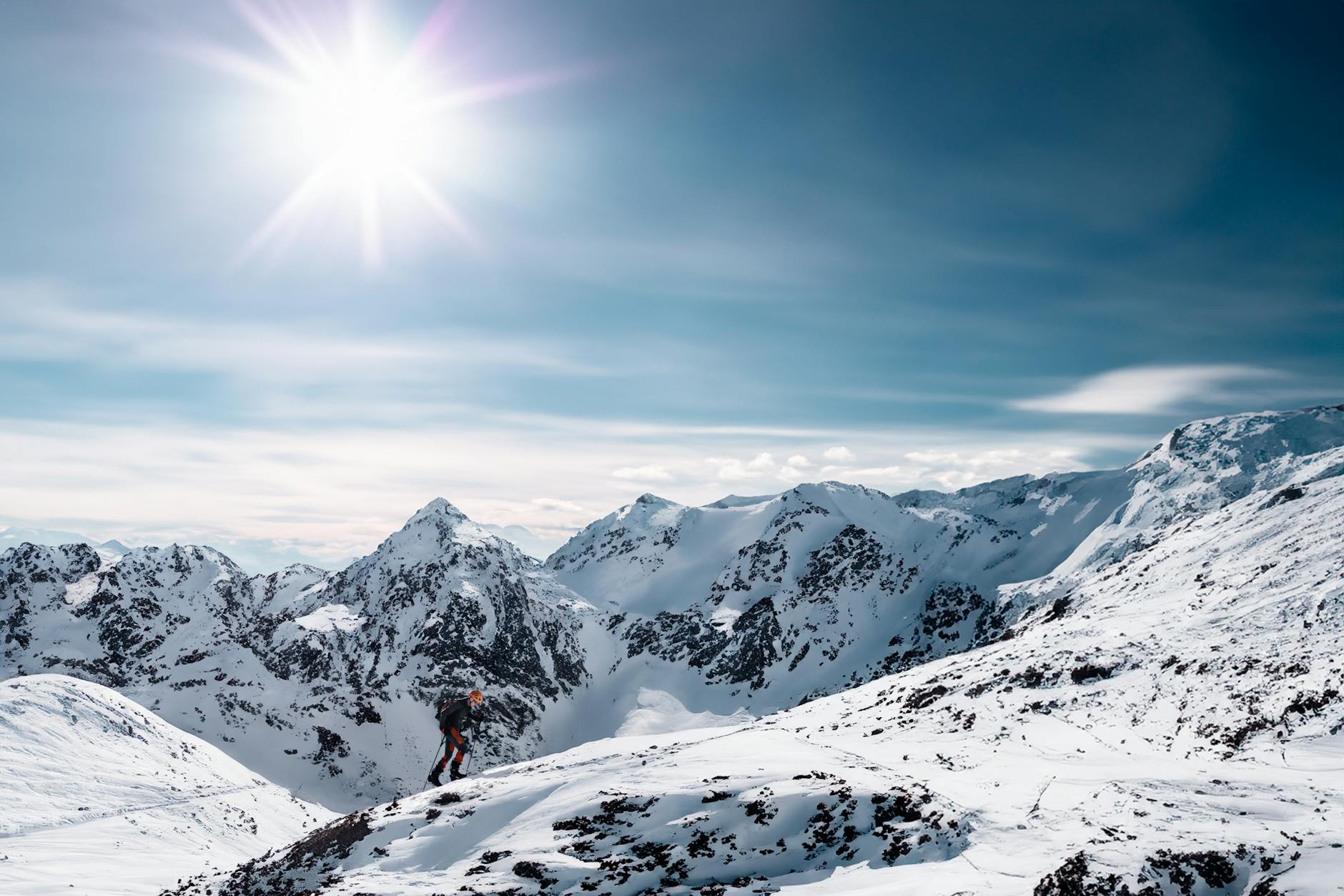 A stunning winter mountain landscape with a solo mountaineer climbing under the bright sun.