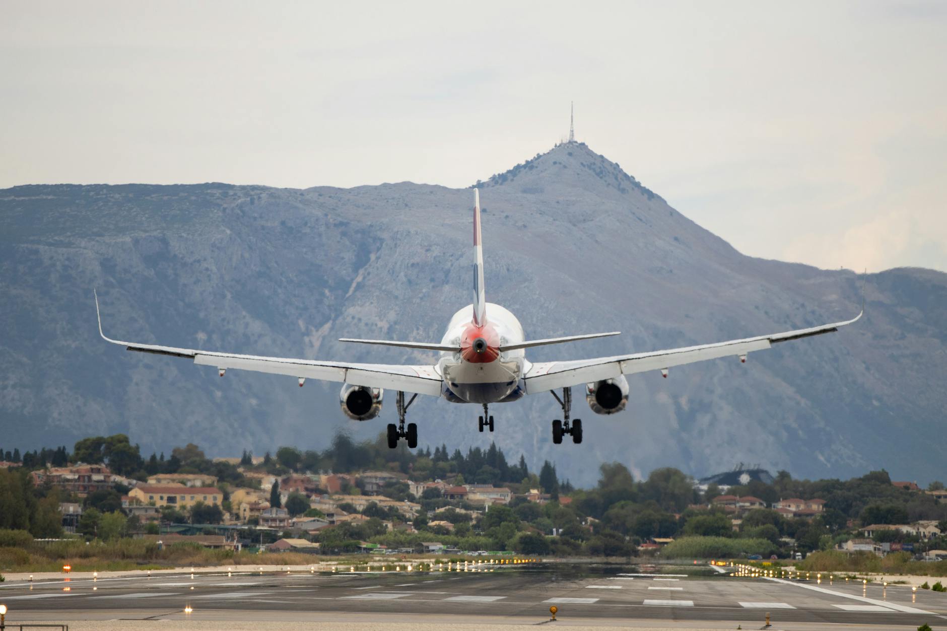 An airplane approaching a runway in Corfu, Greece, set against a mountainous backdrop.