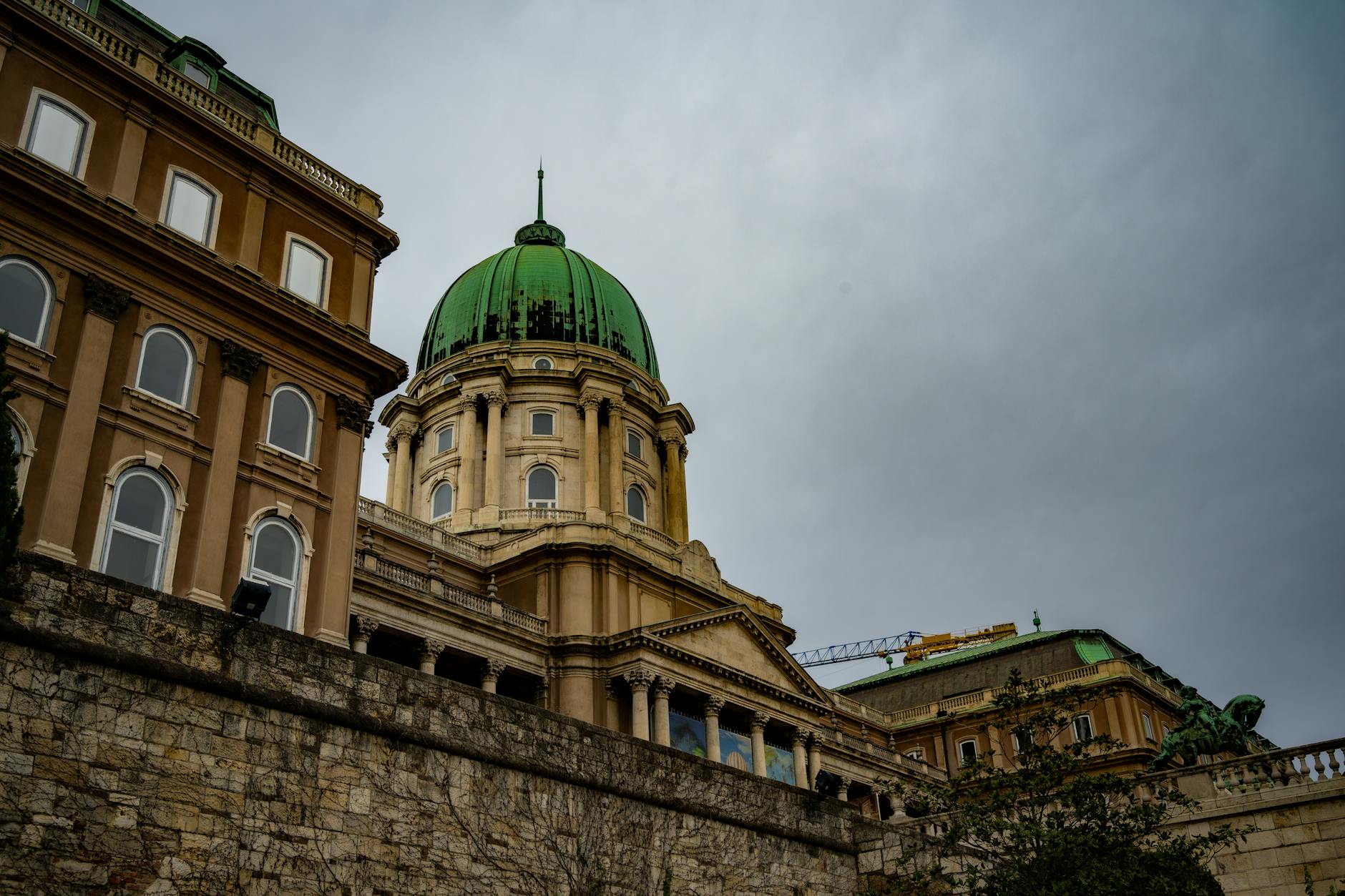 A stunning view of Budapest Castle with its striking architecture and green dome under a cloudy sky.