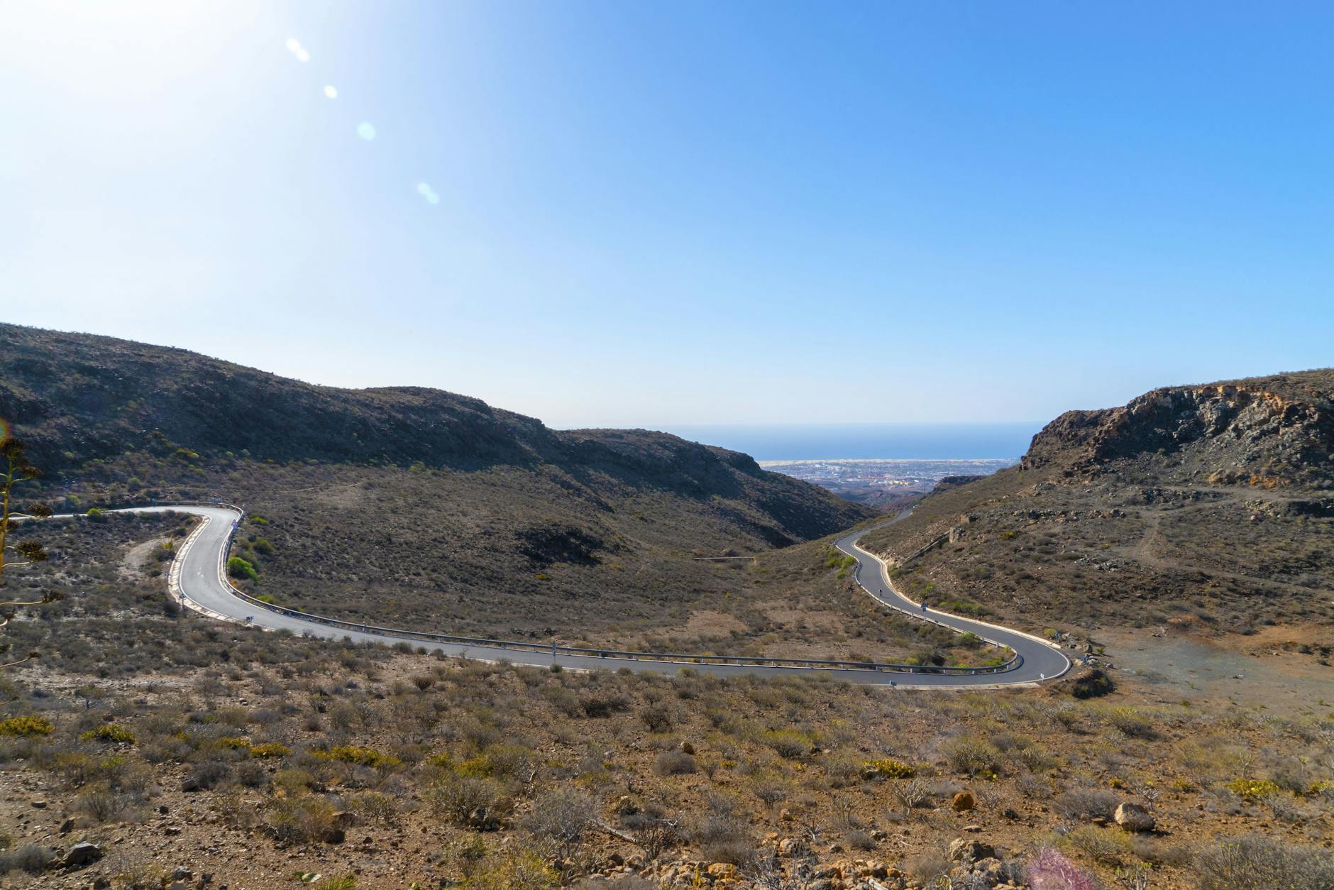 A winding road through the rugged hills of Gran Canaria under a clear summer sky.