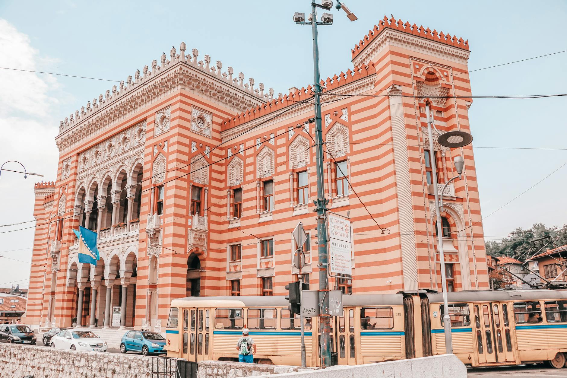 Sarajevo City Hall's historic architecture showcased in this vibrant street scene with a passing tram.