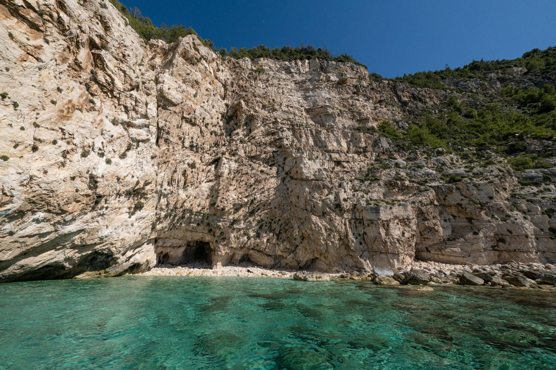 Explore a tranquil seaside cave nestled beneath towering cliffs with turquoise waters.
