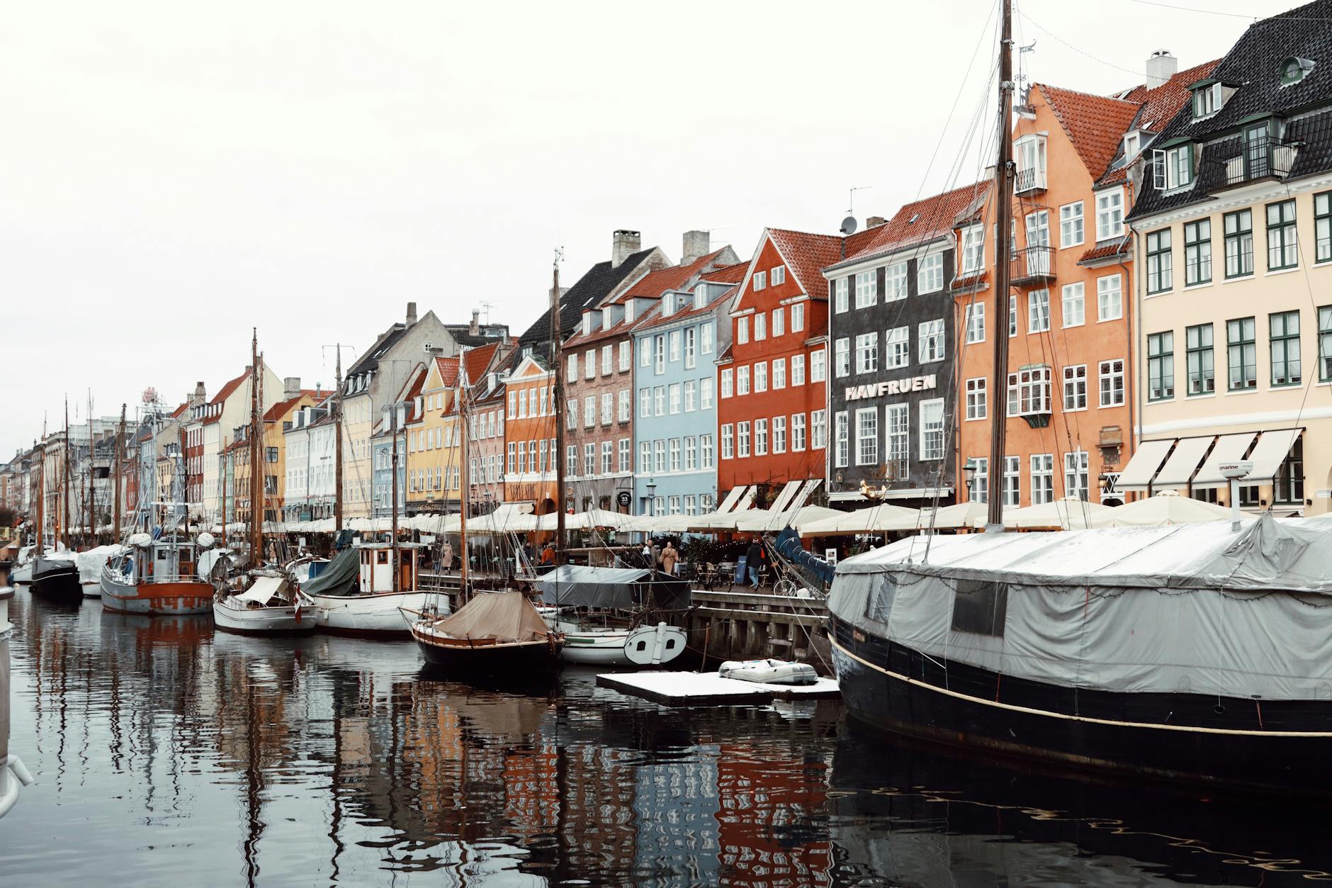 Colorful buildings along Nyhavn Canal in Copenhagen reflecting in the water with moored boats.