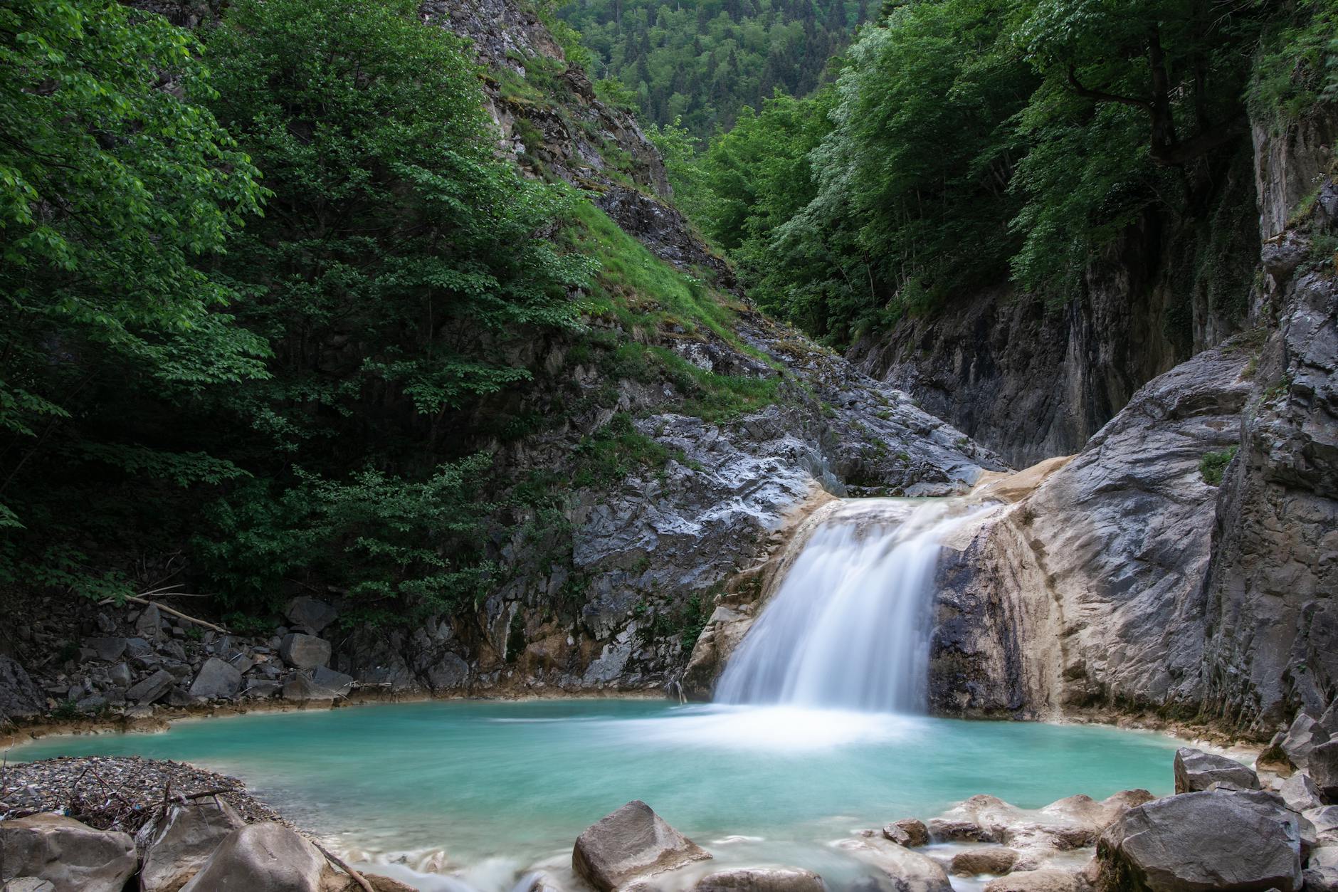 A tranquil waterfall flowing into a turquoise pool surrounded by lush greenery and rocky cliffs.