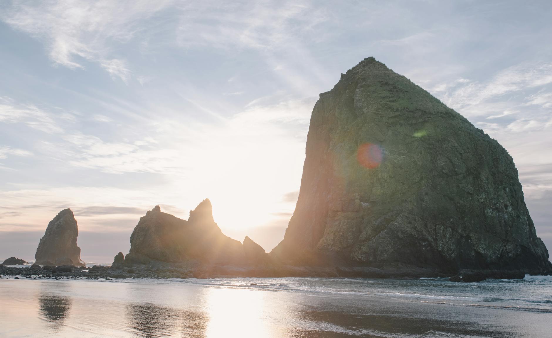 A stunning view of Haystack Rock during sunset on the Oregon coast, reflecting on sandy beach.