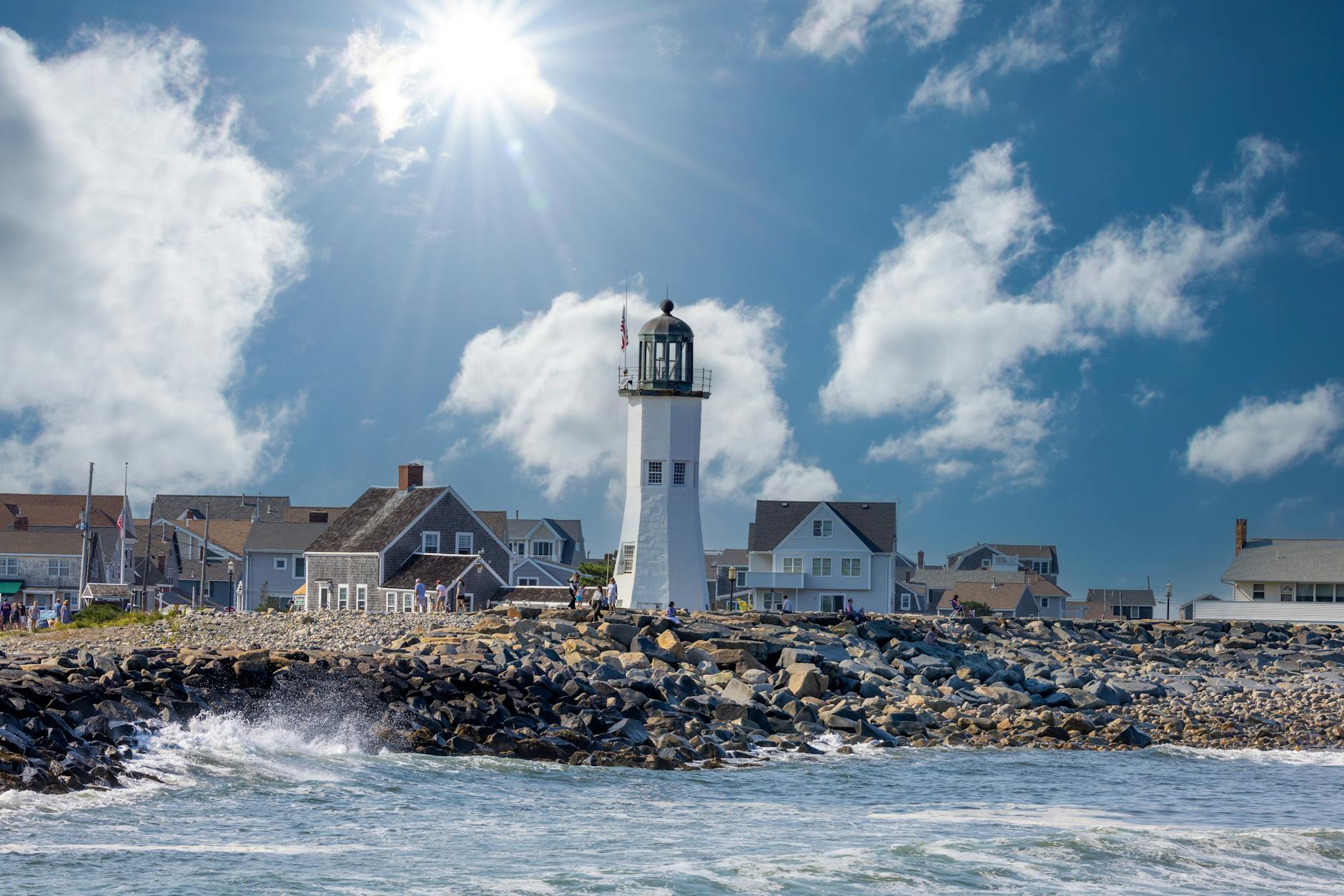 Vibrant view of Gloucester lighthouse with splashing waves and bright sunrays.