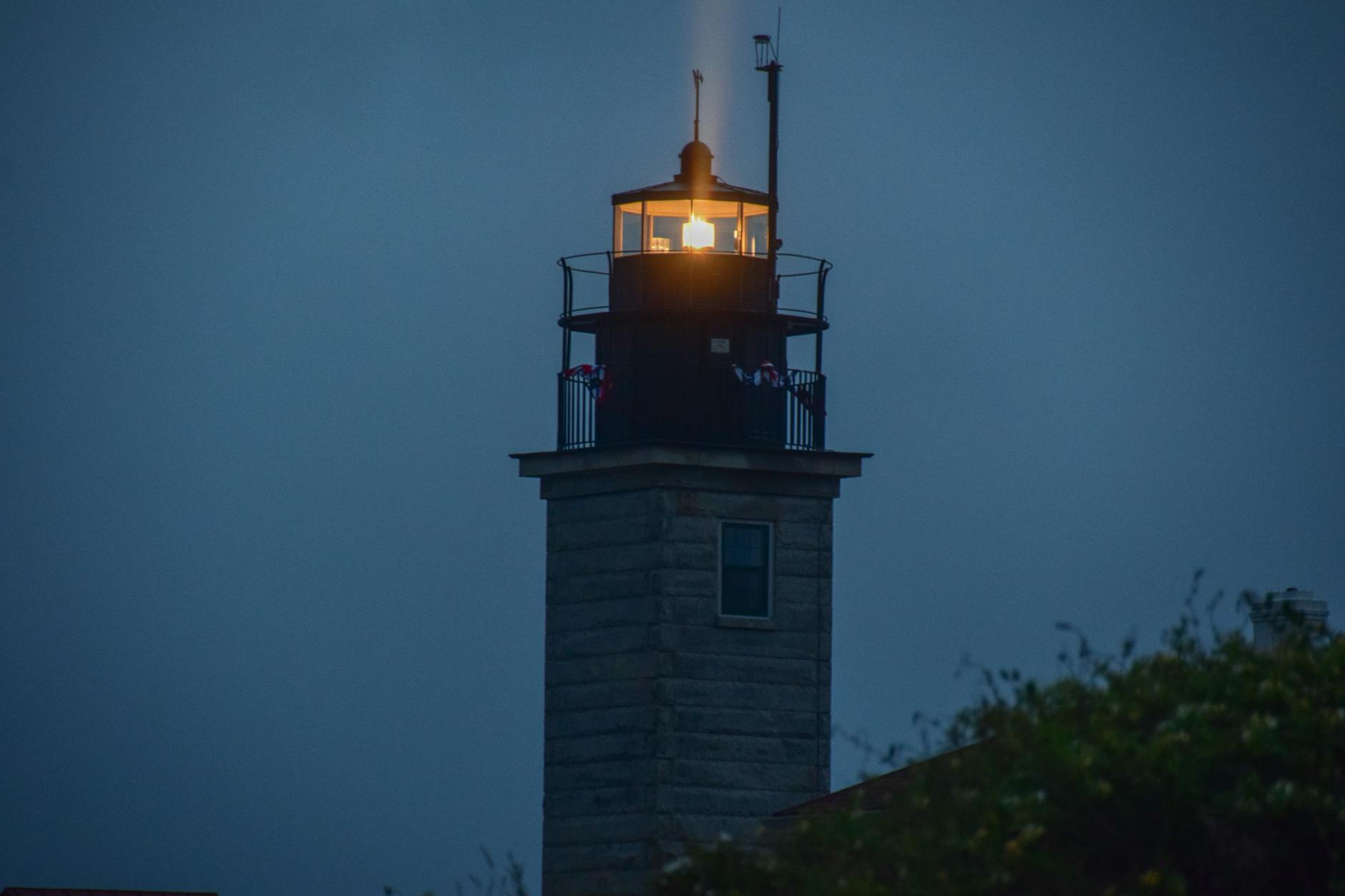 A serene view of Beavertail Lighthouse glowing at night, guiding ships near Jamestown, RI.