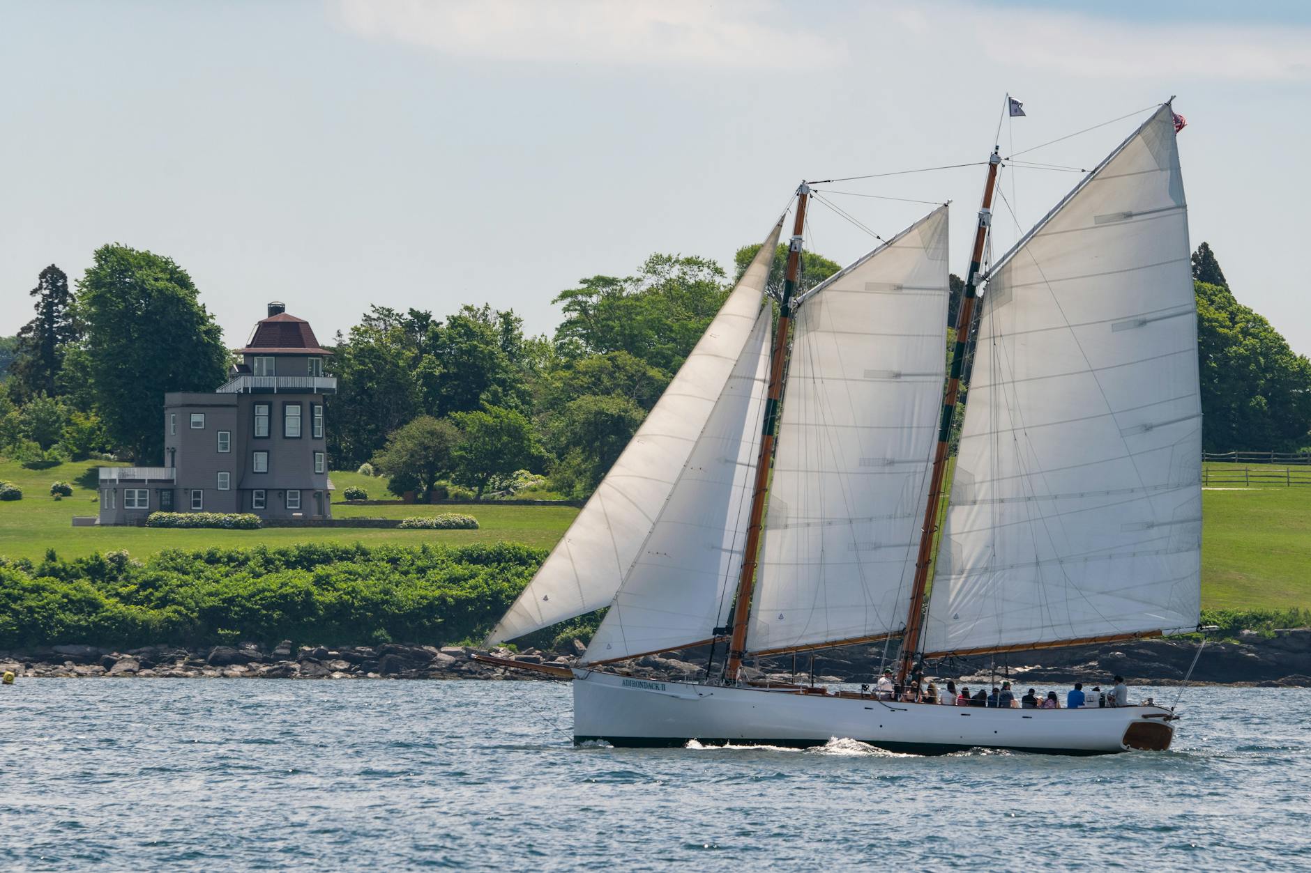 A classic schooner sails past a historic house on a sunny day in Newport, Rhode Island.