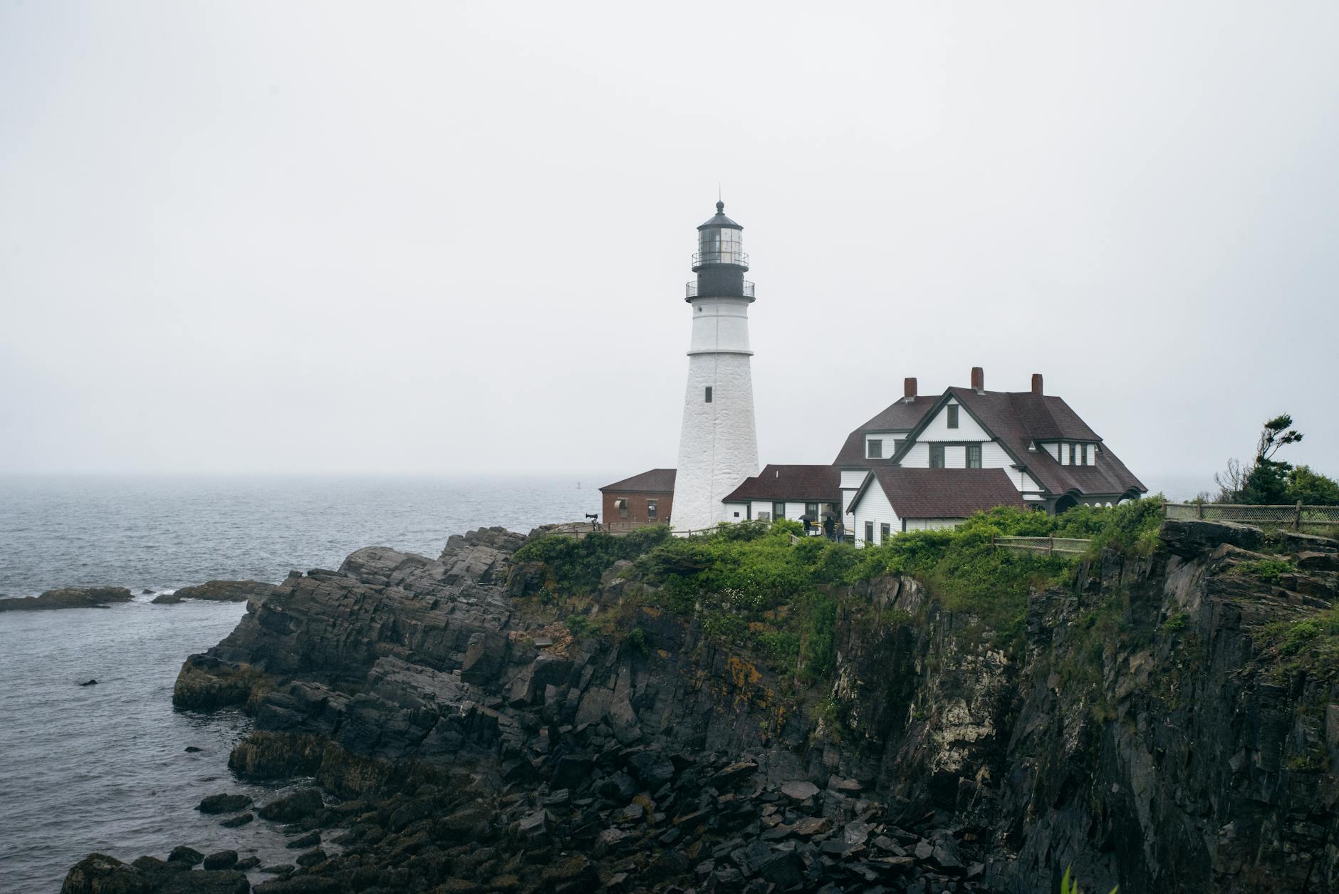 Scenic view of Portland Head Lighthouse with rocky coastline under overcast skies.