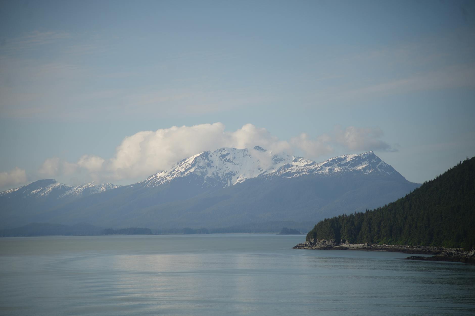 Majestic view of snow-capped Alaskan mountains and tranquil waters under a clear sky.