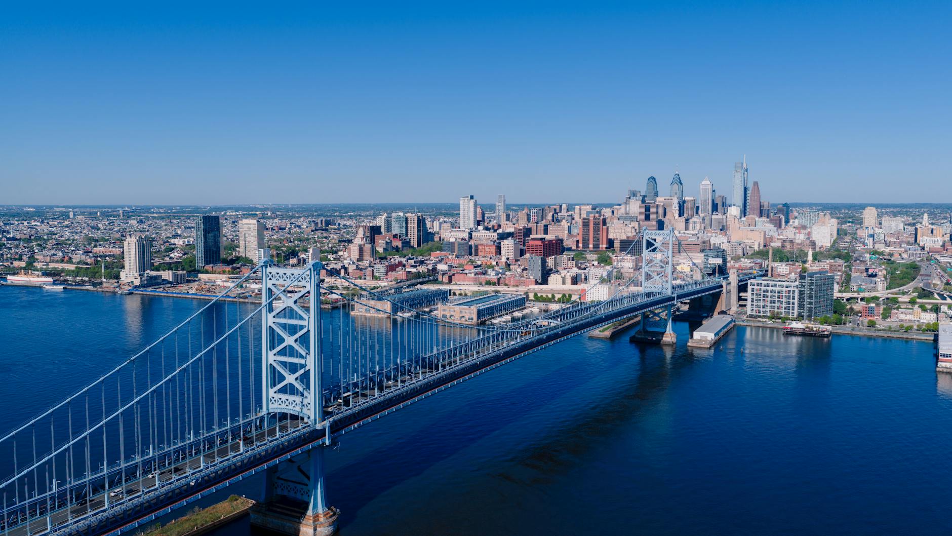 Stunning aerial image of the Ben Franklin Bridge leading into downtown Philadelphia with a clear blue sky.