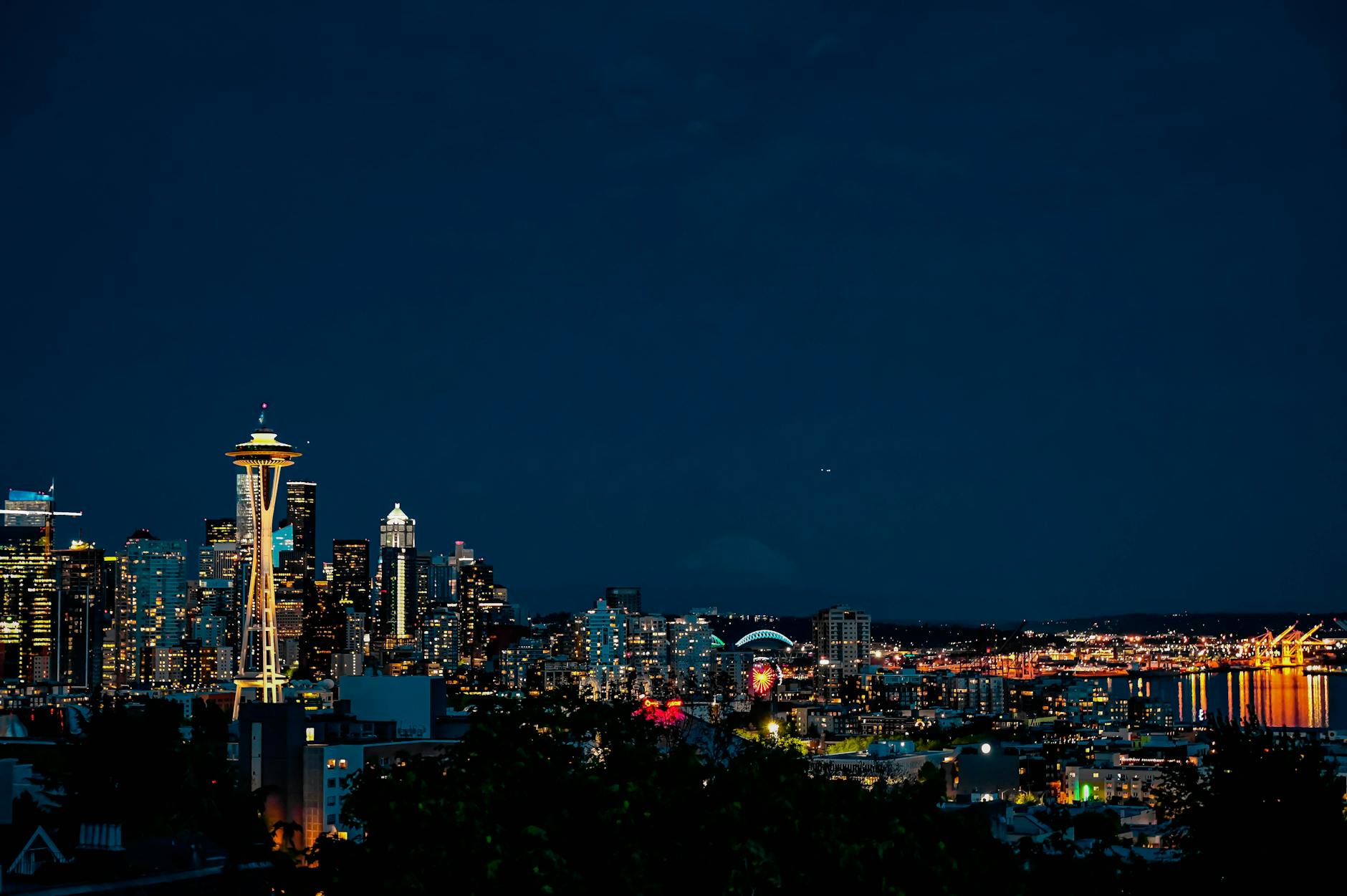 Seattle skyline at night with illuminated Space Needle and city buildings reflecting in water.