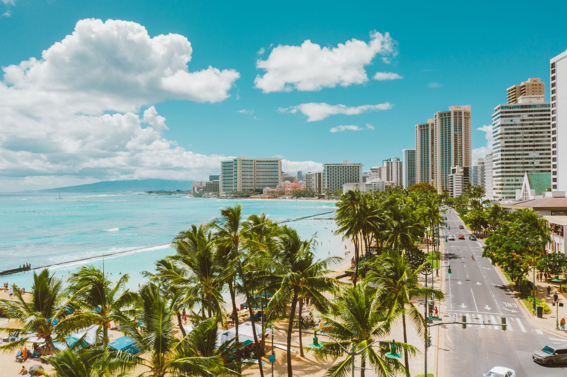 Stunning aerial view of Waikiki Beach, tropical palm trees, and Honolulu skyline under a clear blue sky.