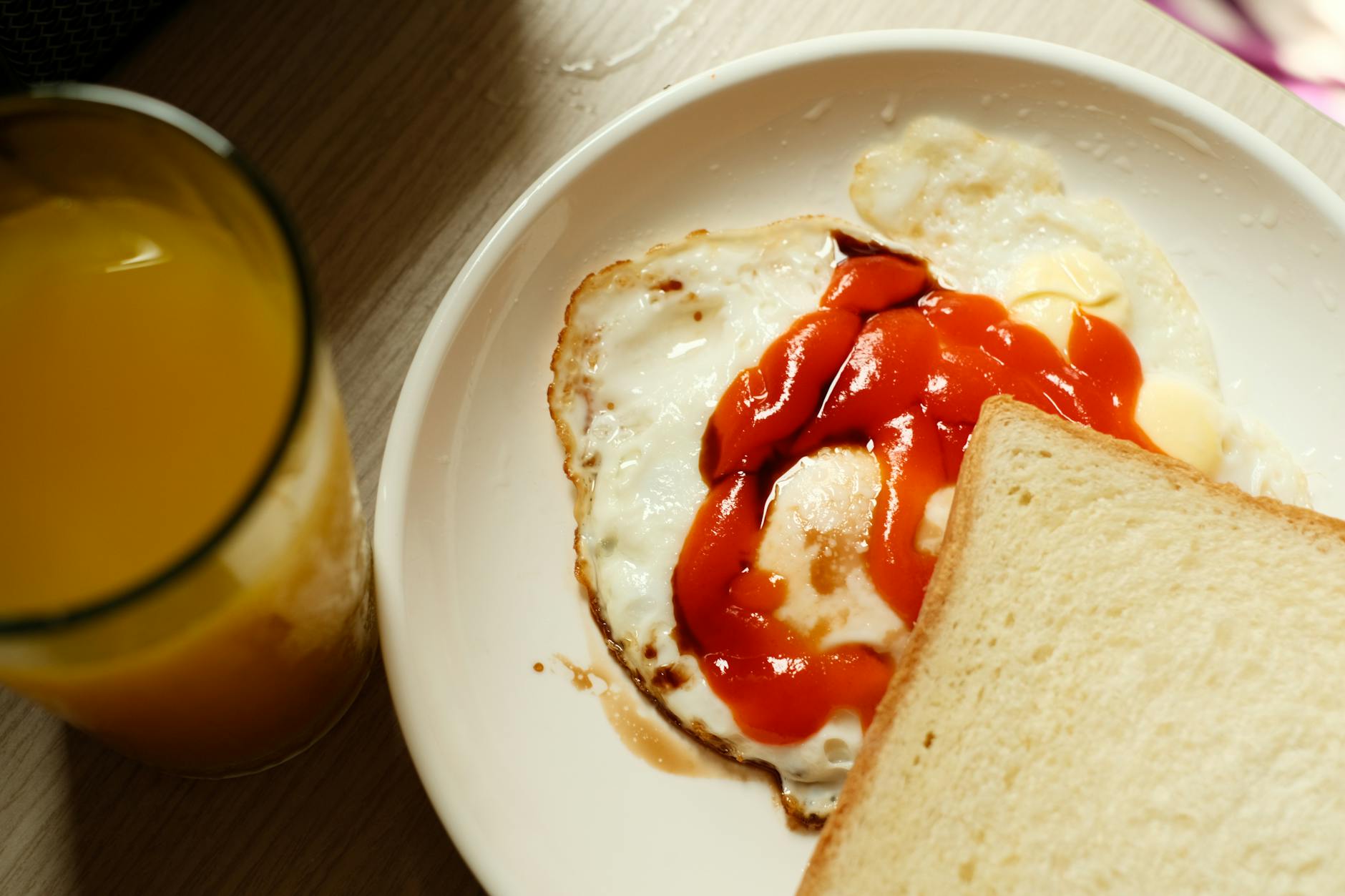 Enjoy a homemade breakfast with sunny side up eggs, ketchup, toast, and orange juice.